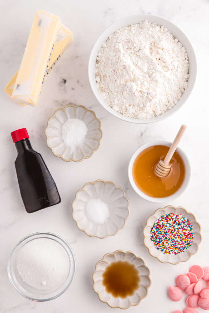 top down image showing all of the ingredients needed for a cookie recipe sitting in small bowls and dishes on a white table top