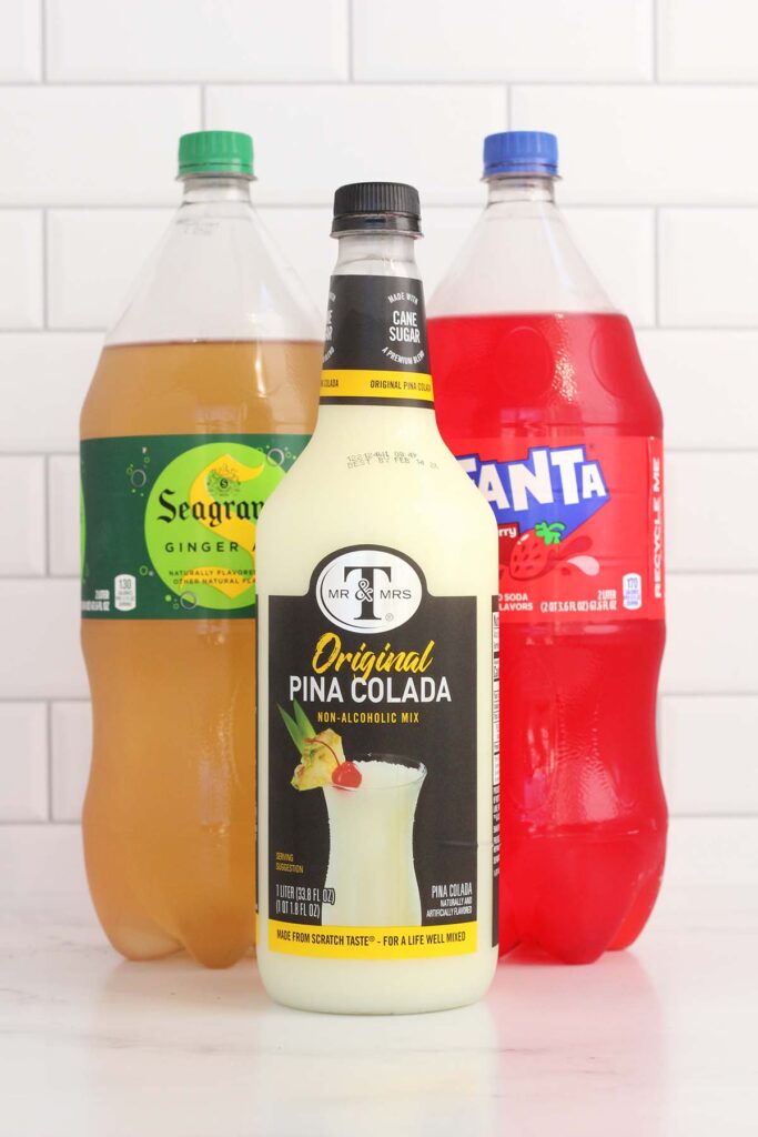 Image showing a bottle of ginger ale, Fanta, and pina colada mix on a white table top with a white subway tile