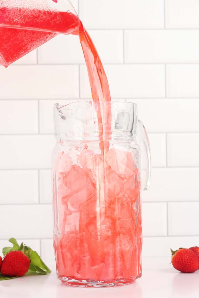 pitcher filled with ice having red soda poured into it