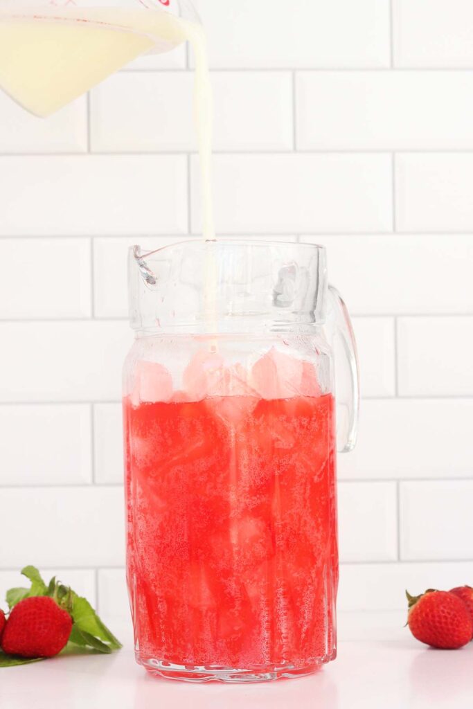 pitcher filled with ice and red soda having a white liquid poured in