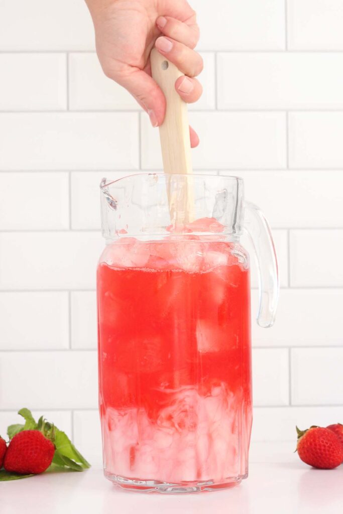 pink and white liquid inside of a pitcher being stirred with a wooden spoon