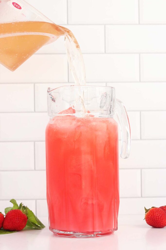 ginger ale being poured into a pitcher with red soda inside