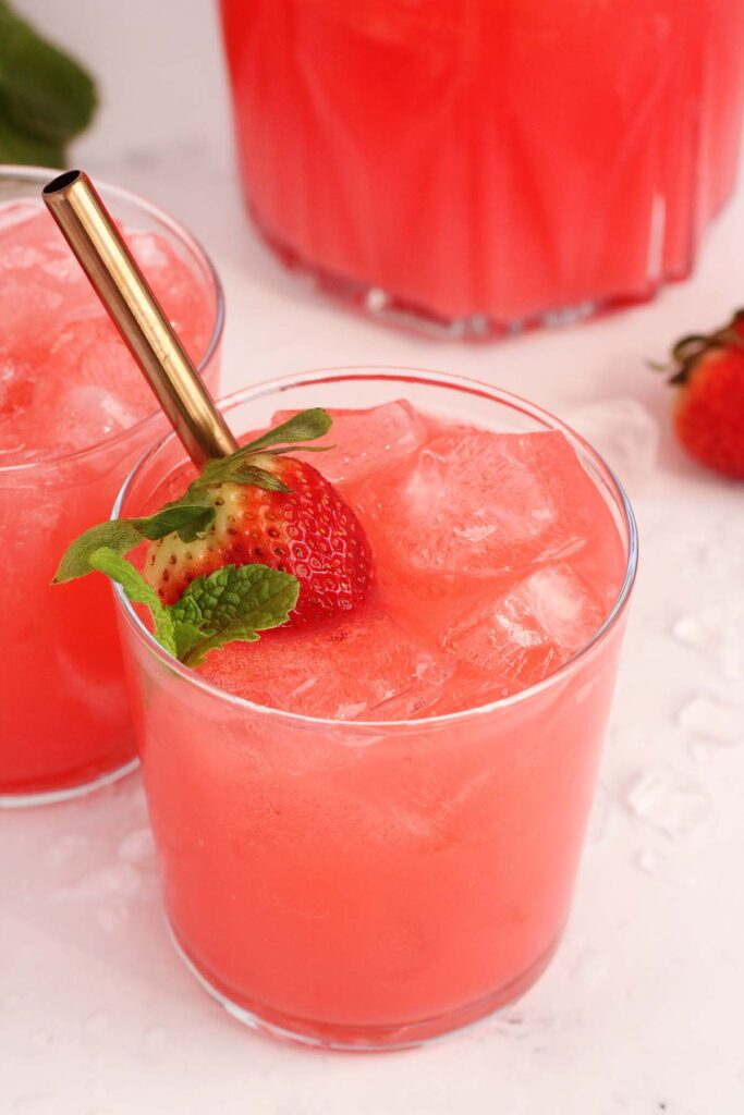 close up image showing a short glass filled with a pink liquid. There is a strawberry and mint with a gold straw inside