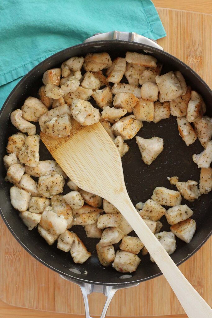 Top down image showing cooked chicken pieces in a skillet with a wooden spoon