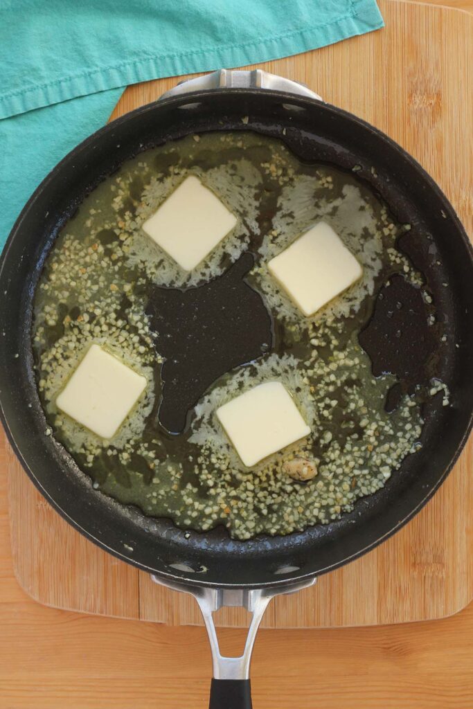 Top down image showing garlic being cooked inside a black skillet with butter