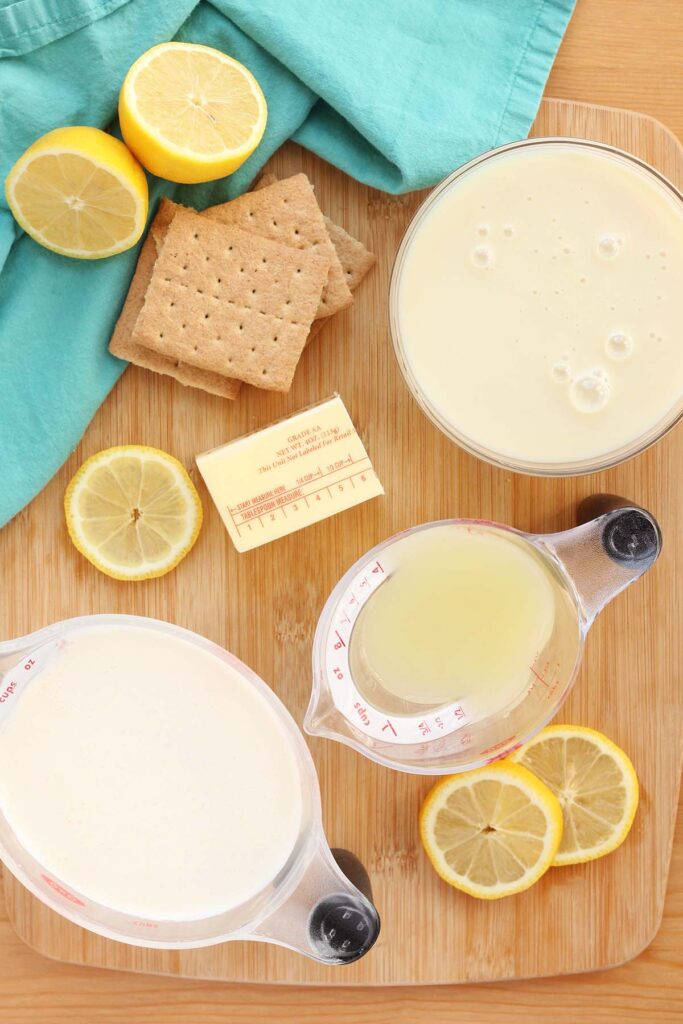 Top down image showing lemons sliced, graham crackers, sweetened condensed milk in a bowl, and lemon juice and cream in measuring cups