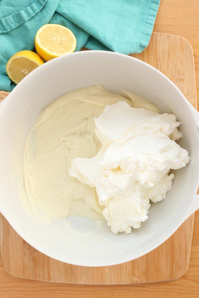 Top down image showing a white mixing bowl with sweetened condensed milk  and a yellow spatula with whipped cream on top