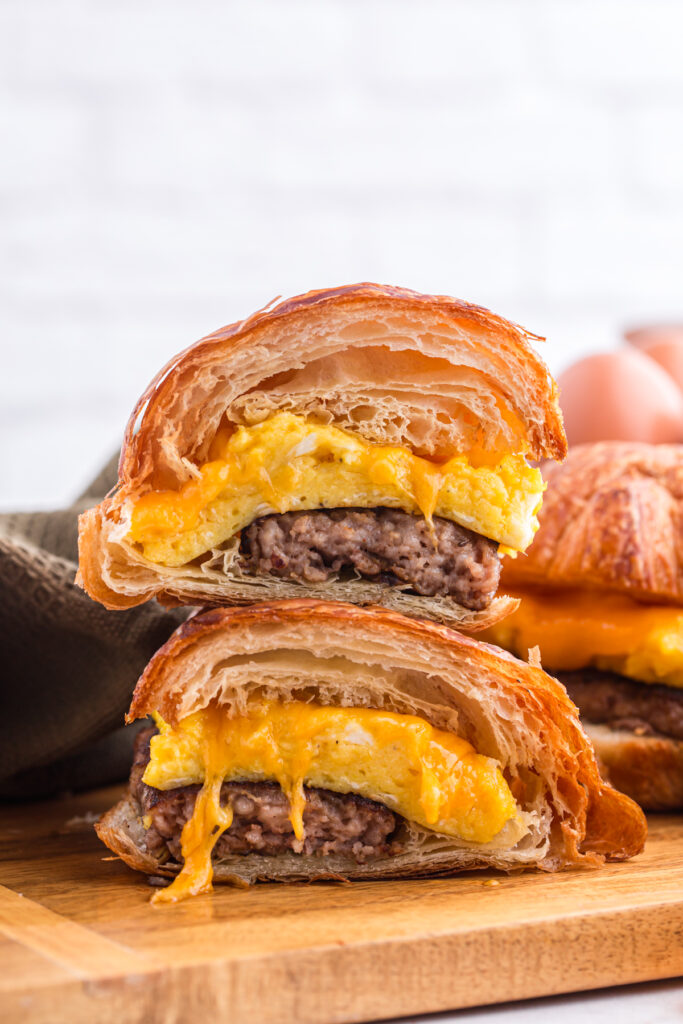 close up image showing a croissant egg sandwich sliced in half with the halves stacked on top of each other