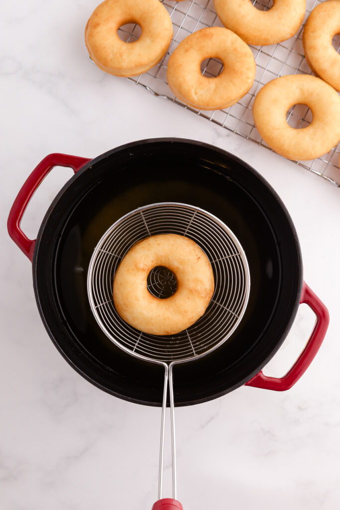 Top down image showing a fried donut being pulled out of oil with a slotted spoon