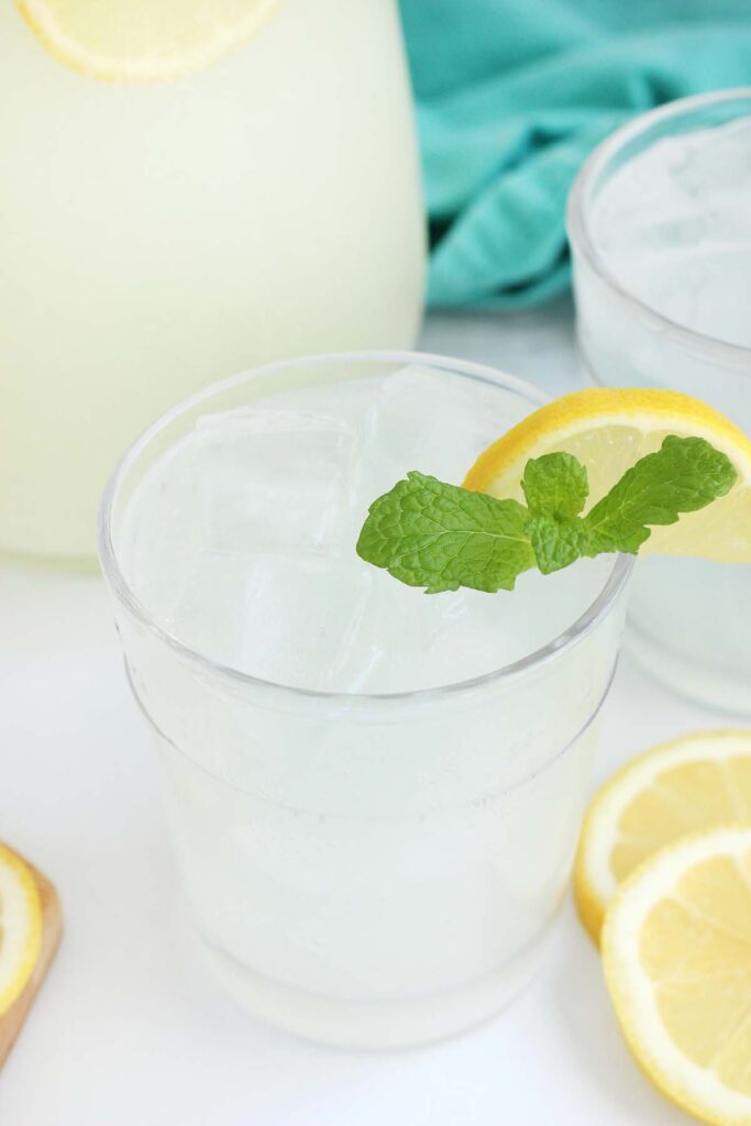 close up of a short glass filled with a light yellow liquid, ice, lemon slices, and mint