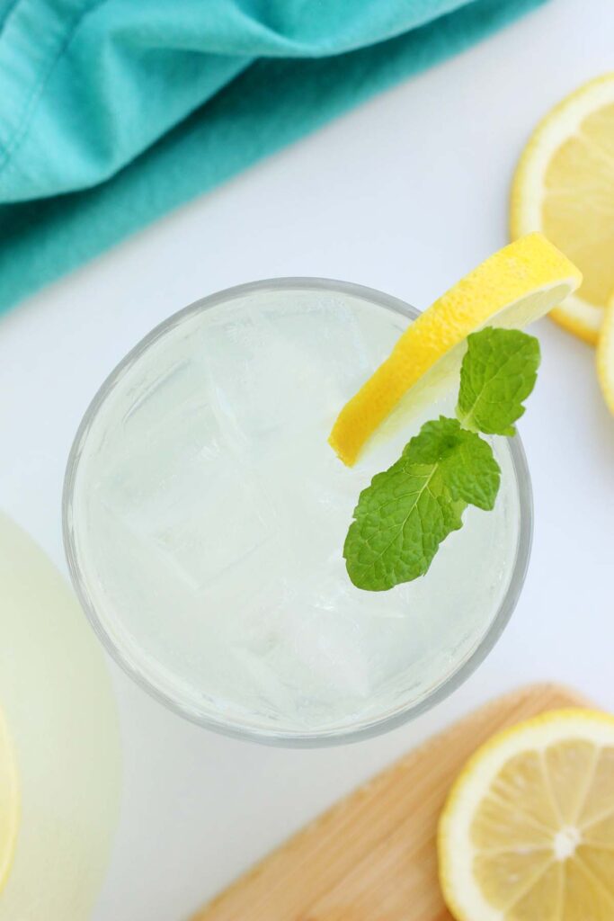 close up of a short glass filled with a light yellow liquid, ice, lemon slices, and mint