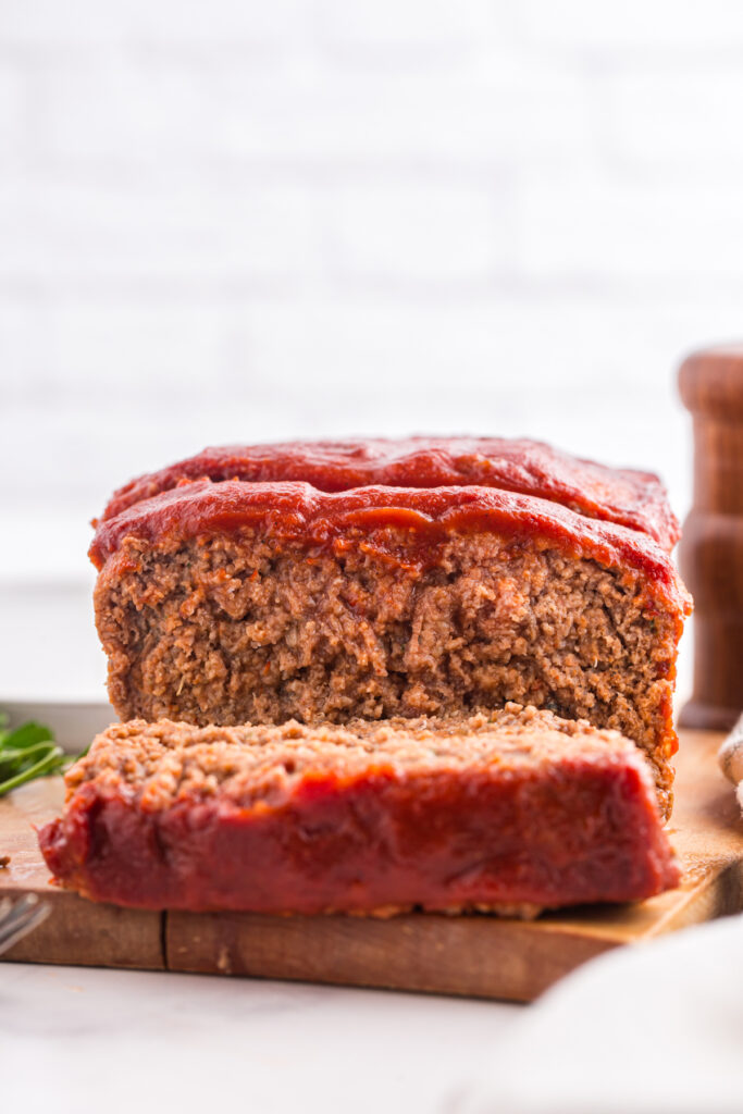 close up image showing meatloaf with a slice taken out on a wooden cutting board