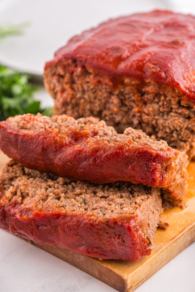 
close up image showing meatloaf with a slice taken out on a wooden cutting board

