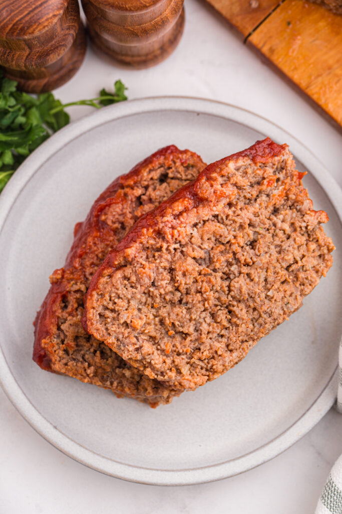 Top down image showing a whtie round plate with two slices of meatloaf stacked on top