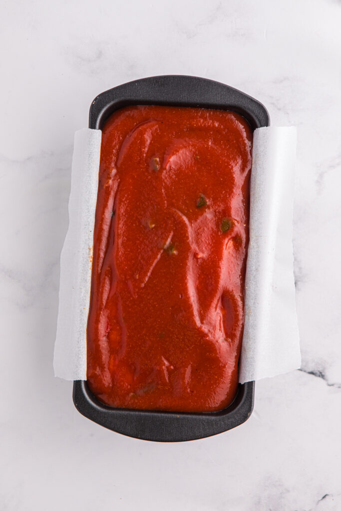 top down image showing a black loaf pan filled with a meat mixture topped with sauce