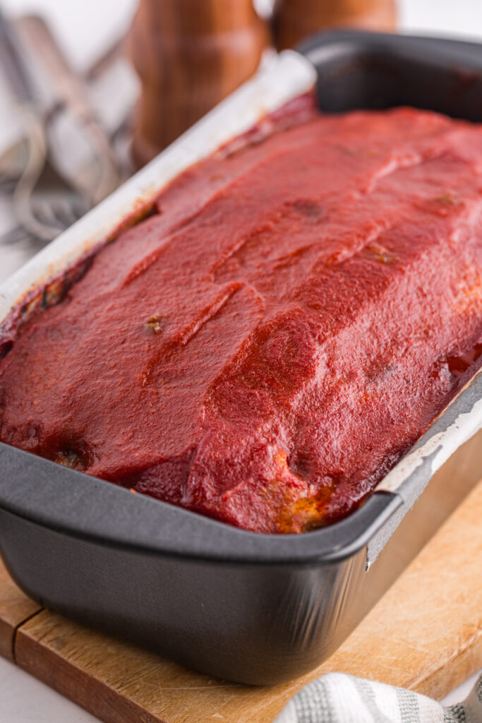 top down image showing a black loaf pan filled with a meat mixture topped with sauce