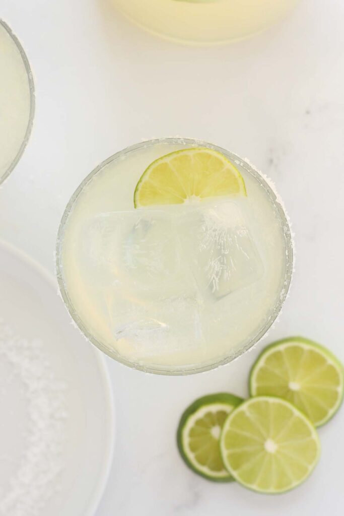 close up image of a margarita glass filled with ice and cocktail with a rimmed edge and lime wedges