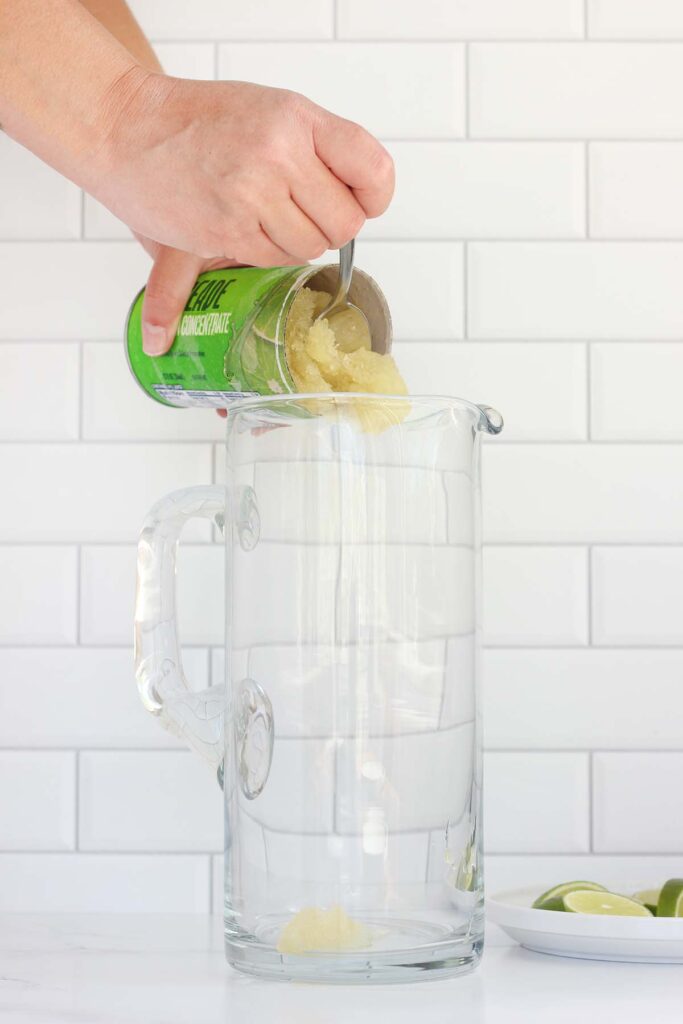 limeade concentrate being poured into a pitcher with lime wedges off to the side