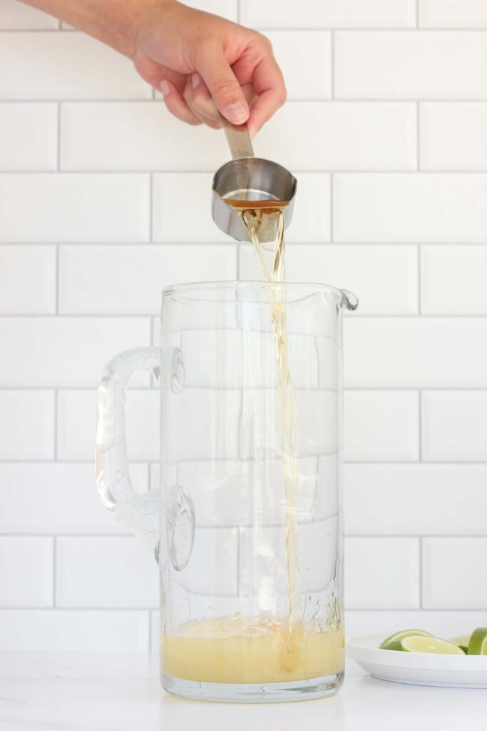 orange liquor being poured into a pitcher with lime wedges off to the side