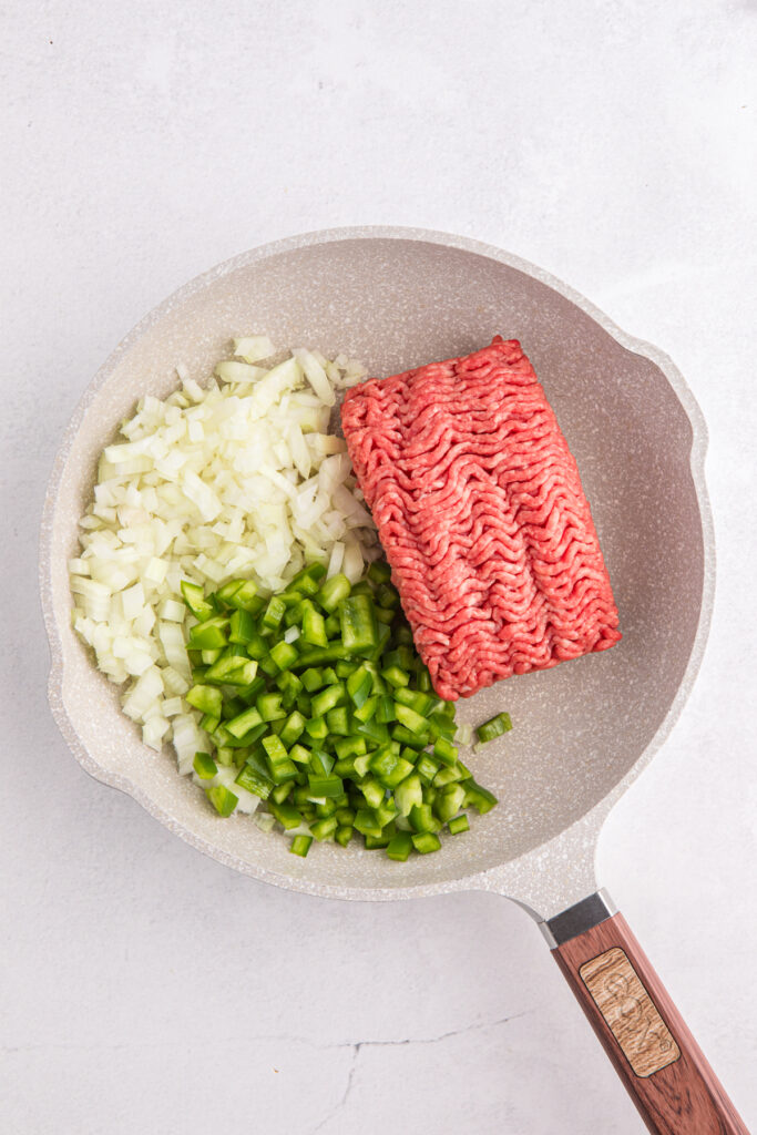 top down image showing uncooked ground beef with chopped onion and green pepper in a pan