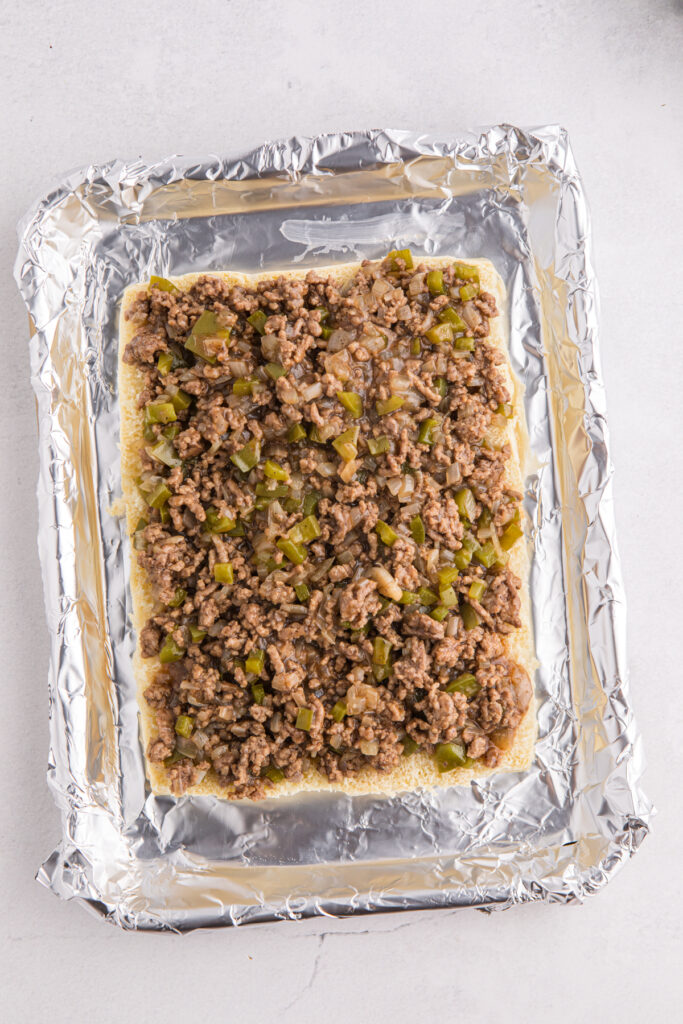 Top down image showing a pan lined with foil with buns, ground beef, and peoppers