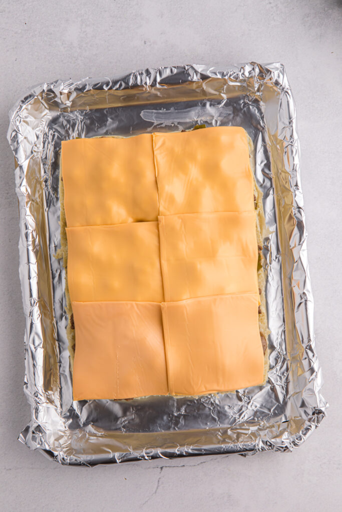 Top down image showing a pan lined with foil with buns topped with ground beef and cheese