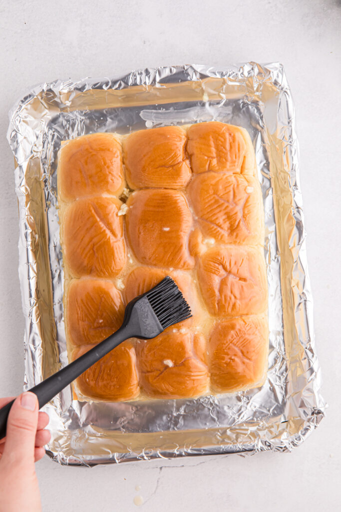 Top down image showing a pan lined with foil with buns being brushed with garlic