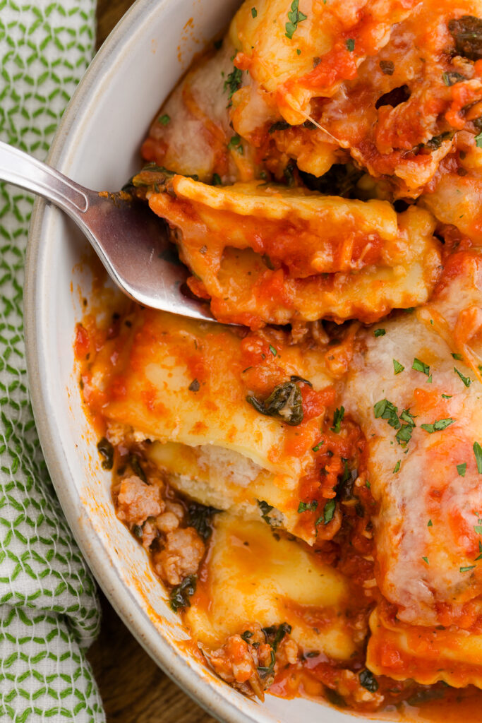 Top down image showing a bowl filled with ravioli and sauce with a bite on a spoon. 