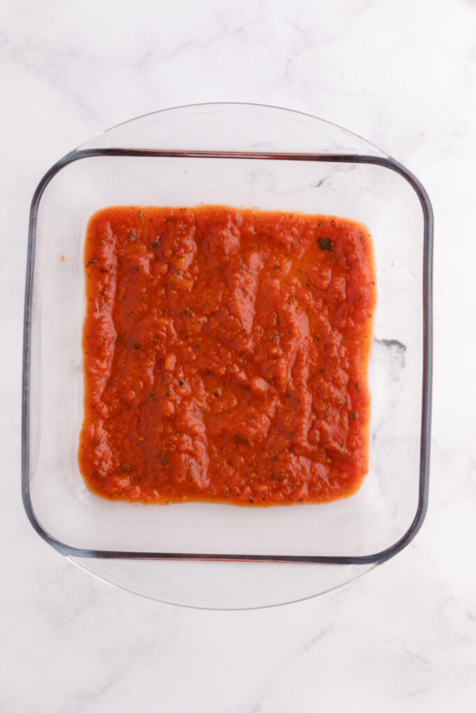 Top down image showing a glass square dish filled with pasta sauce