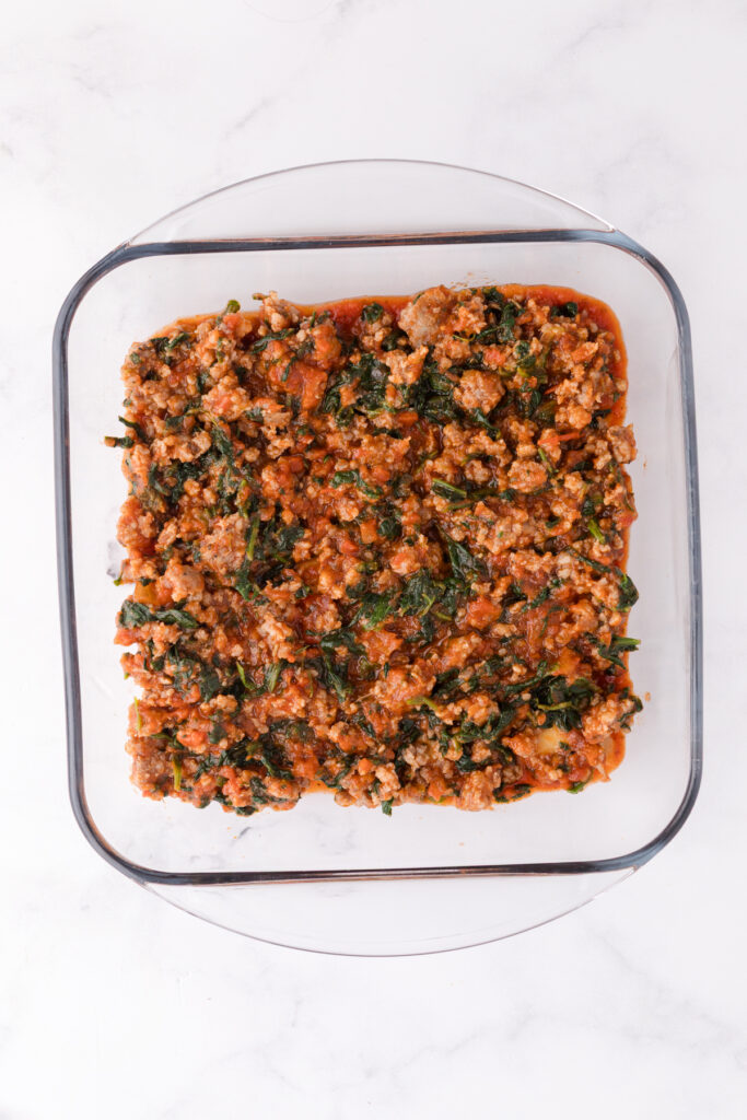 Top down image showing a glass square dish filled with pasta sauce and beef