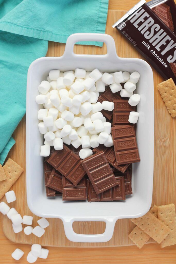 Top down image showing a white rectangle baking dish with hershey's chocolate pieces and marshmallows stacked inside