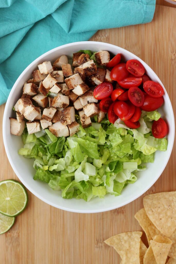 Top down image showing a white serving bowl filled with lettuce, tomatoes and chicken 