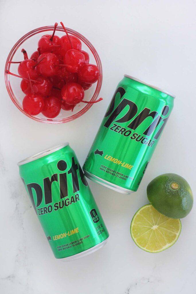 Top down image showing two sprite zero sugar cans with cherries in a bowl and a lime cut in half