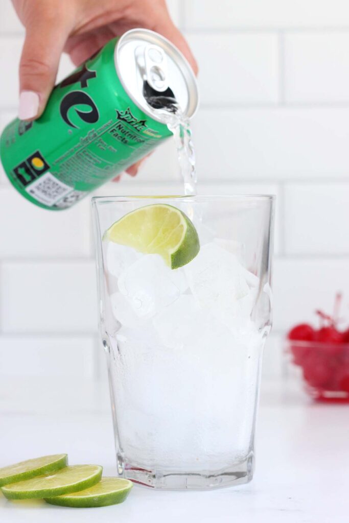 sprite being poured into a glass filled with ice and a lime wedge