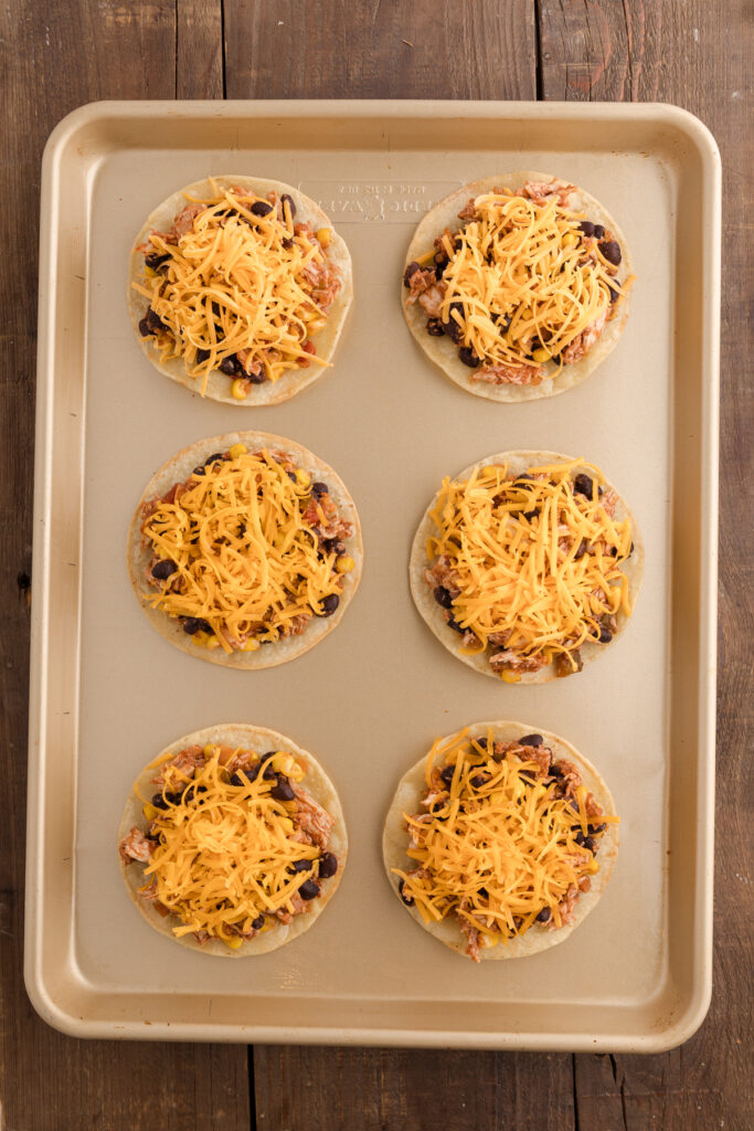 top down image showing a tray of corn tortillas topped with a chicken and bean mixture with cheese
