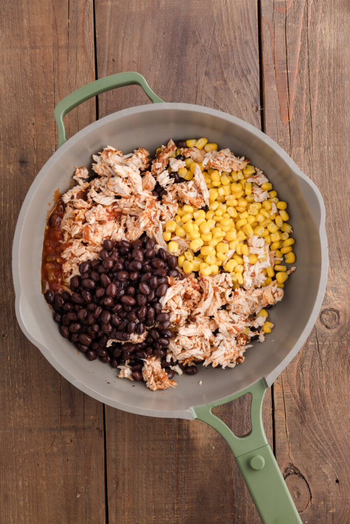top down image showing shredded chicken, salsa, corn, and black beans unmixed in a pan