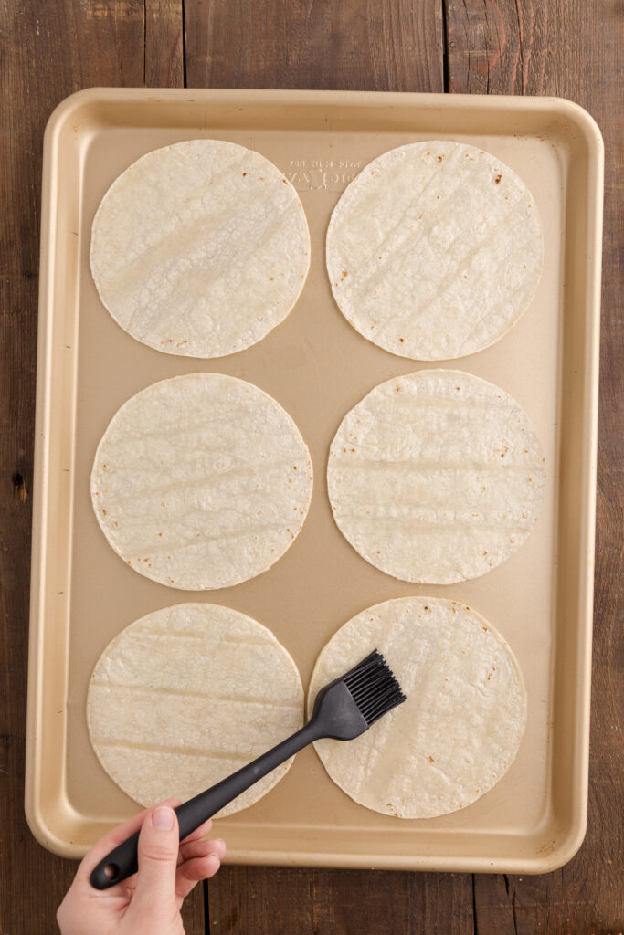 top down image showing a tray of corn tortillas being brushed with oil