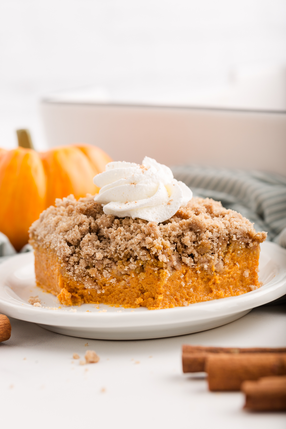 close up image showing what looks like pumpkin pie with a crumb topping on a white plate topped with whipped cream