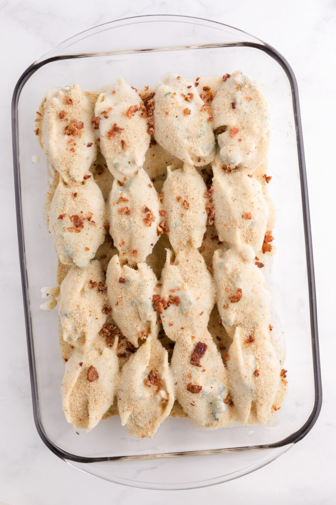 Top down image showing filled shells sitting in a glass baking dish topped with sauce and bacon