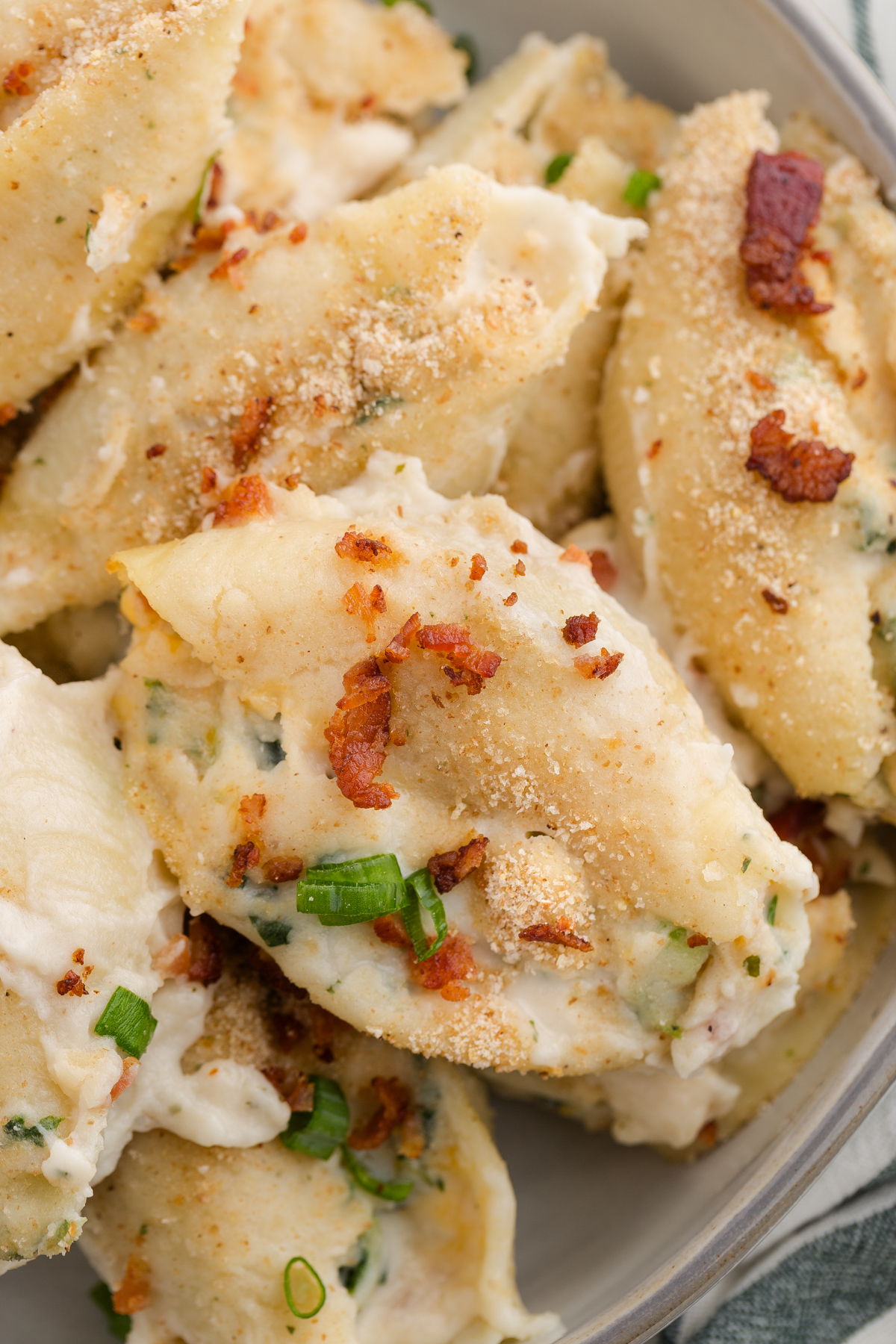 close up image showing a stuffed shell with crispy bacon and a white sauce