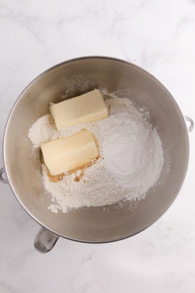 Top down image showing the inside of a mixing bowl filled with flour, powdered sugar, and butter unmixed