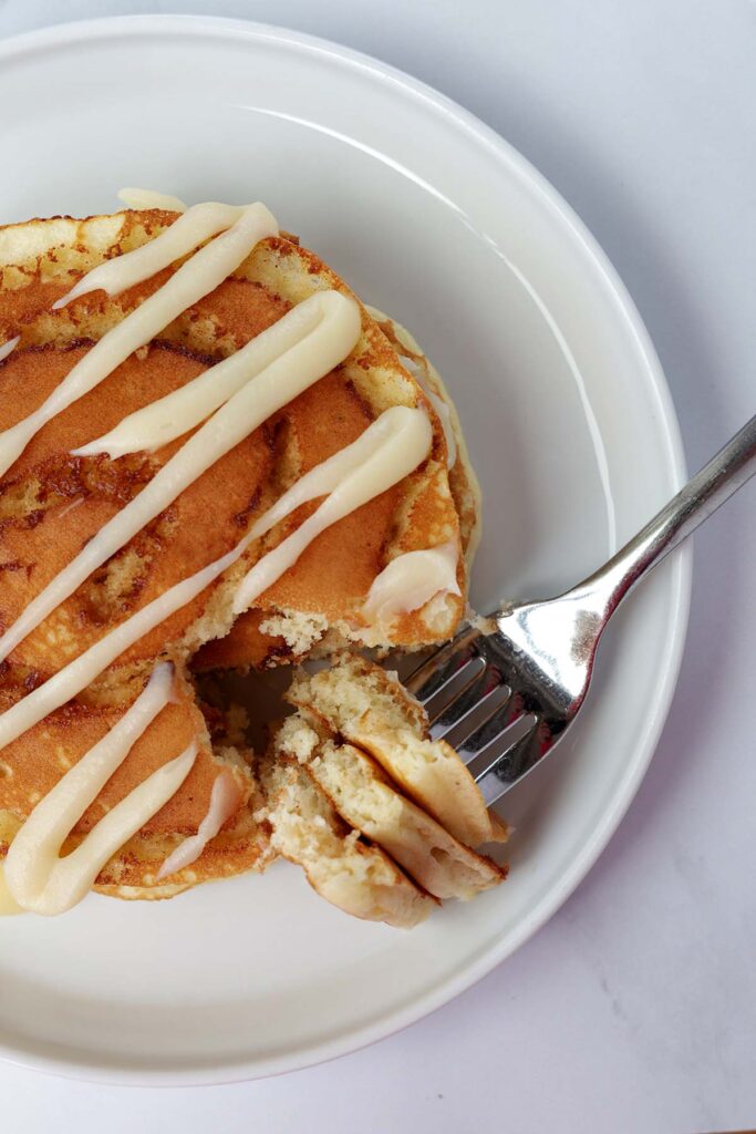 top down image showing a close up of a pancake that has a glaze drizzled and a bite cut out on a fork