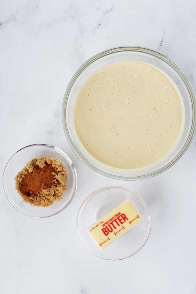 top down imgae showing a bowl of pancake batter, a bowl of cinnamon and brown sugar, and a stick of butter