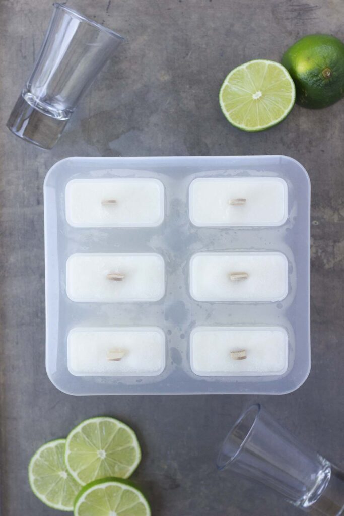 Top down image showing a close up of a popsicle mold filled with white liquid with lime slices off to the side