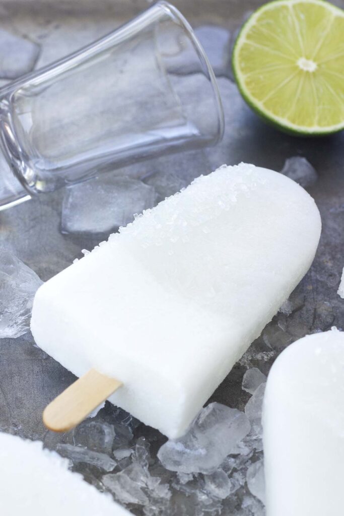 Top down image showing a white popsicle on top of broken ice pieces with lime slices in the background