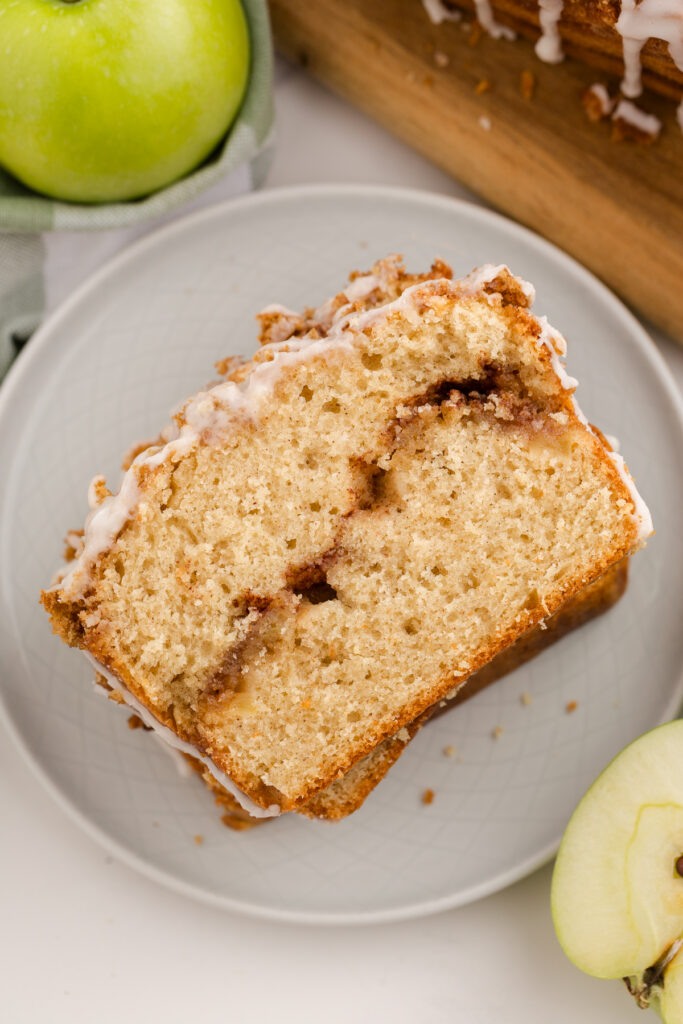 close up image showing a sweet bread in slices leaning against one another with a cinnamon swirl through the middle and a glaze on top with green apples in the background