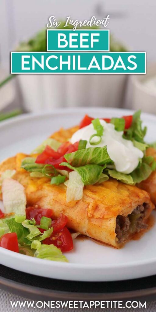 close up image showing a single enchilada sliced in half topped with lettuce, tomato, and sour cream on a white plate
