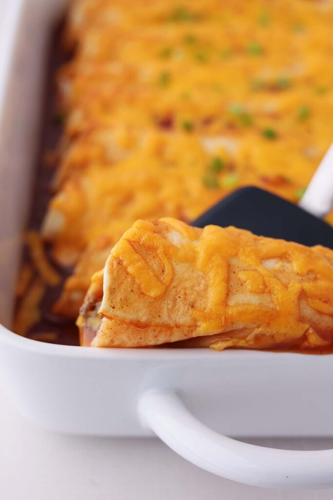 close up of a spatula pulling an enchilada out of a white baking dish