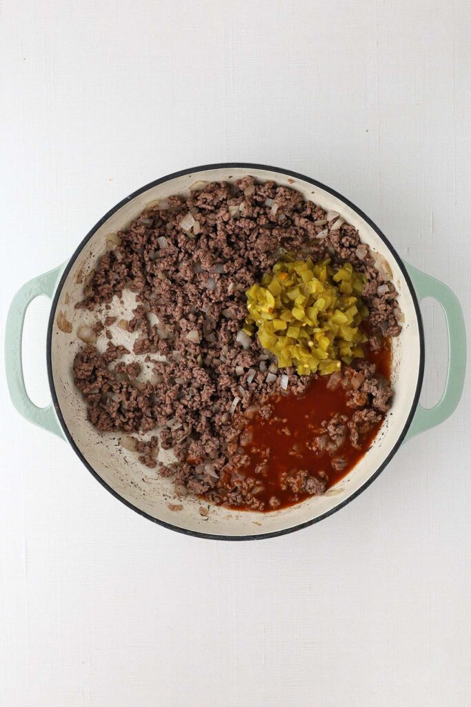 top down image showing a skillet with cooked ground beef, green chilies and enchilada sauce