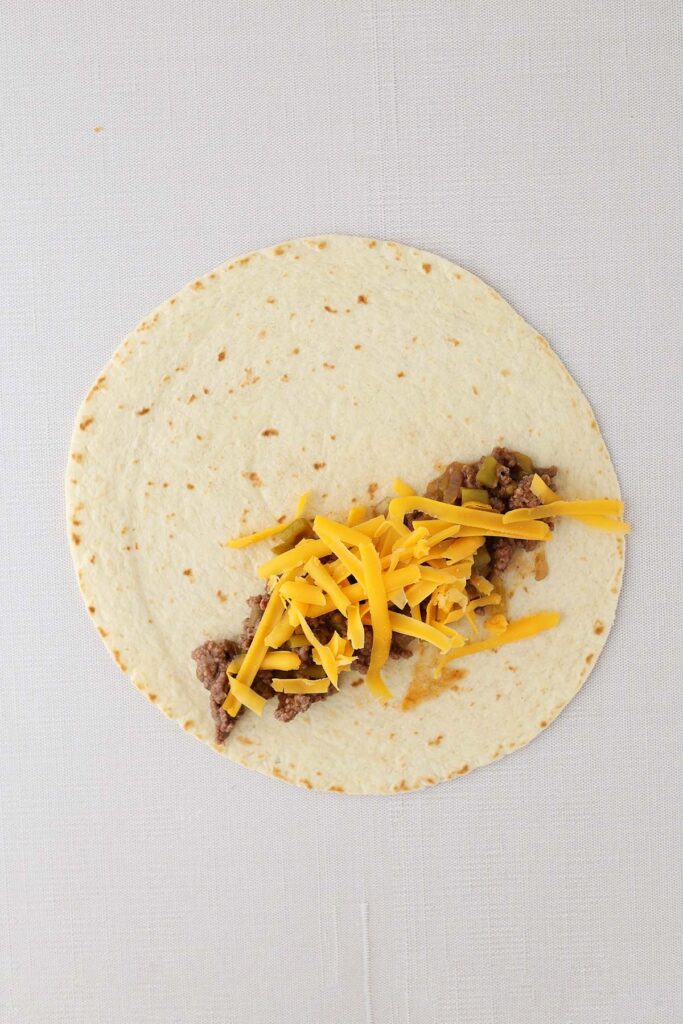 Top down image showing a tortilla with beef and cheese on top